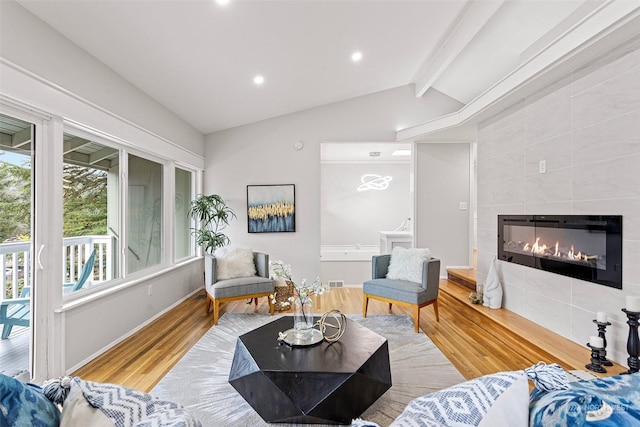 living room featuring a tiled fireplace, vaulted ceiling with beams, and light hardwood / wood-style flooring