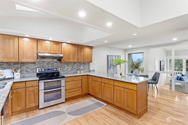 kitchen with appliances with stainless steel finishes, vaulted ceiling with skylight, tasteful backsplash, light stone countertops, and kitchen peninsula