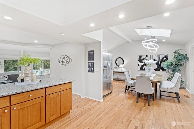 dining space with lofted ceiling with skylight, a chandelier, and light wood-type flooring