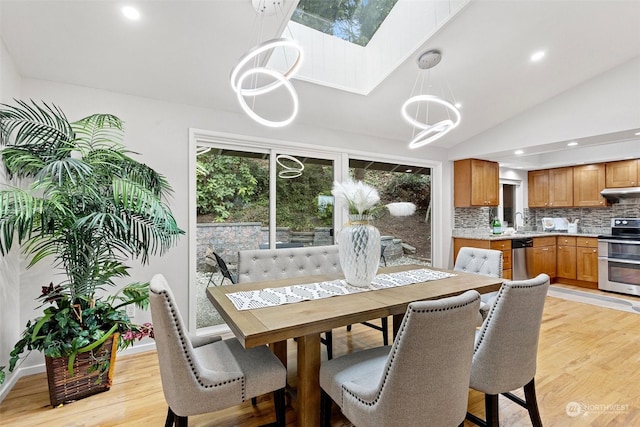 dining room featuring a notable chandelier, light hardwood / wood-style flooring, lofted ceiling with skylight, and sink