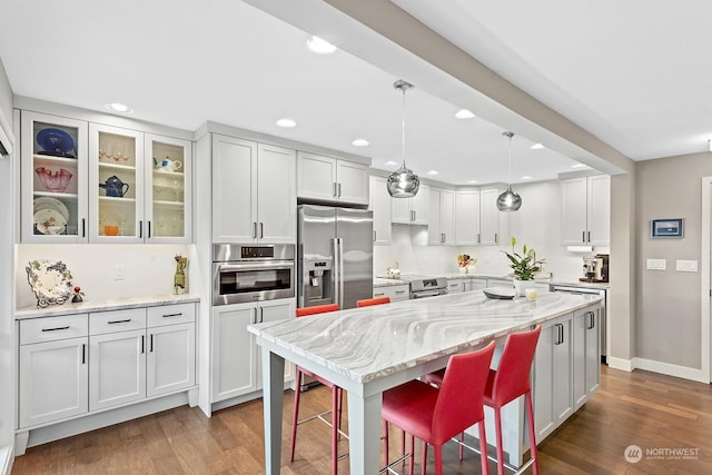 kitchen with a kitchen bar, a center island, appliances with stainless steel finishes, light stone countertops, and white cabinets