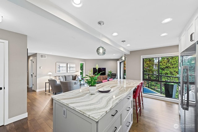 kitchen featuring decorative light fixtures, stainless steel fridge, a kitchen island, light stone countertops, and white cabinets