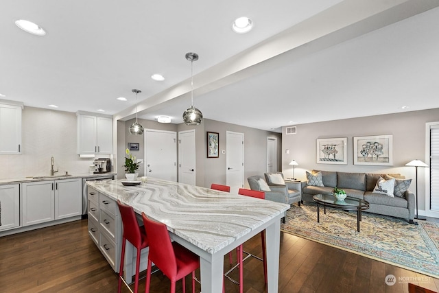 kitchen featuring white cabinetry, sink, a breakfast bar area, hanging light fixtures, and light stone countertops