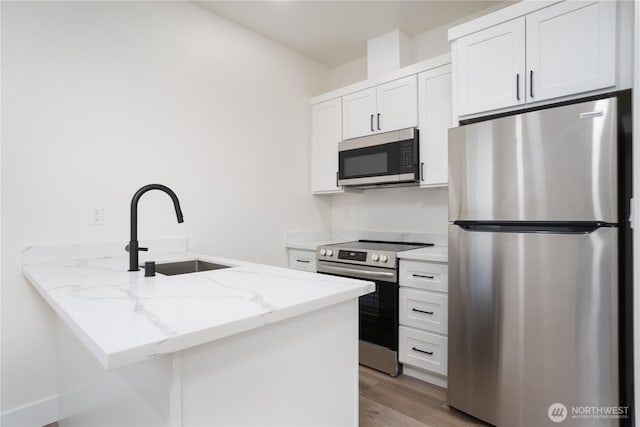 kitchen featuring light stone counters, a sink, stainless steel appliances, light wood finished floors, and a peninsula