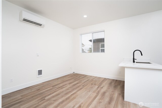 spare room featuring light wood finished floors, visible vents, an AC wall unit, a sink, and baseboards