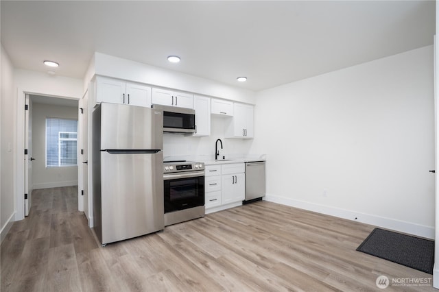 kitchen featuring white cabinets, light wood-style flooring, a sink, baseboards, and appliances with stainless steel finishes