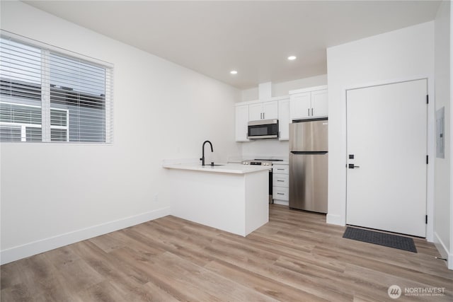 kitchen with a peninsula, a sink, light wood-type flooring, baseboards, and appliances with stainless steel finishes