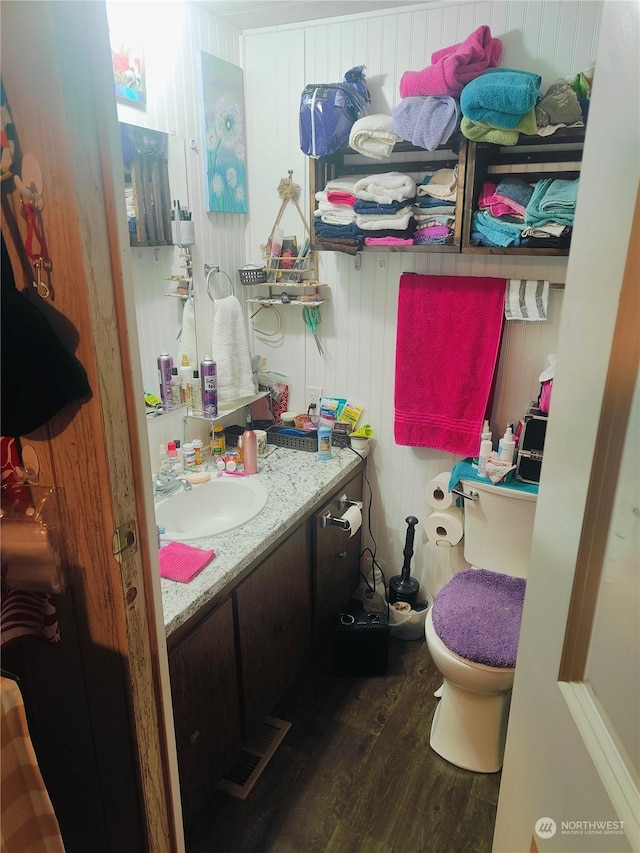 bathroom with wooden walls, wood-type flooring, toilet, and vanity