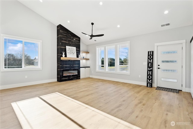 unfurnished living room featuring ceiling fan, a large fireplace, high vaulted ceiling, and light hardwood / wood-style floors