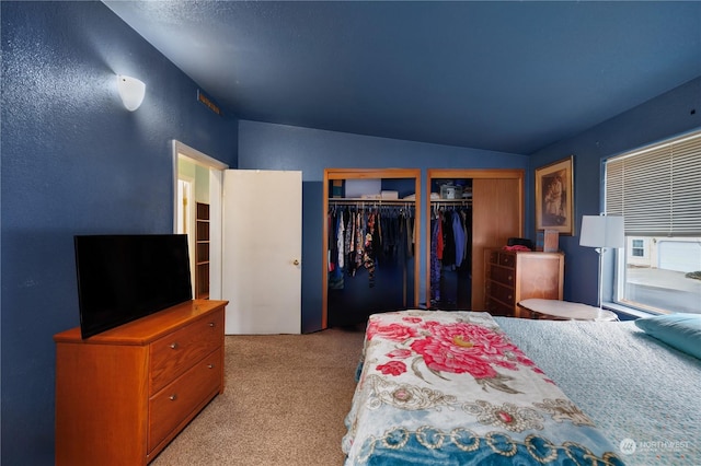 carpeted bedroom with lofted ceiling and multiple closets