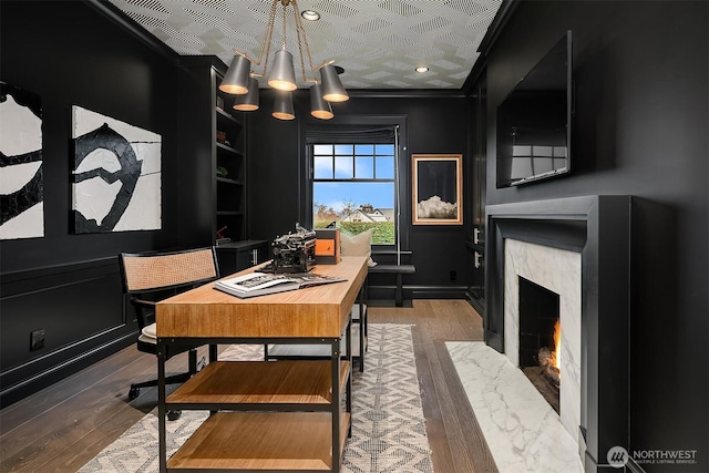 dining space with built in shelves, a decorative wall, ornamental molding, a high end fireplace, and wood finished floors