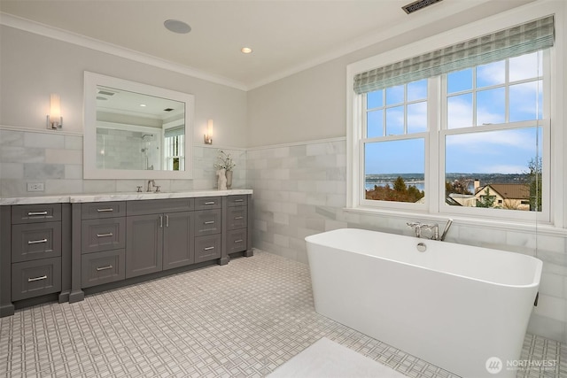 bathroom featuring tile walls, recessed lighting, a freestanding bath, ornamental molding, and vanity