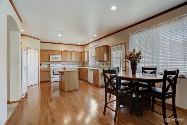 kitchen featuring white appliances, a kitchen island, decorative backsplash, light hardwood / wood-style floors, and ornamental molding