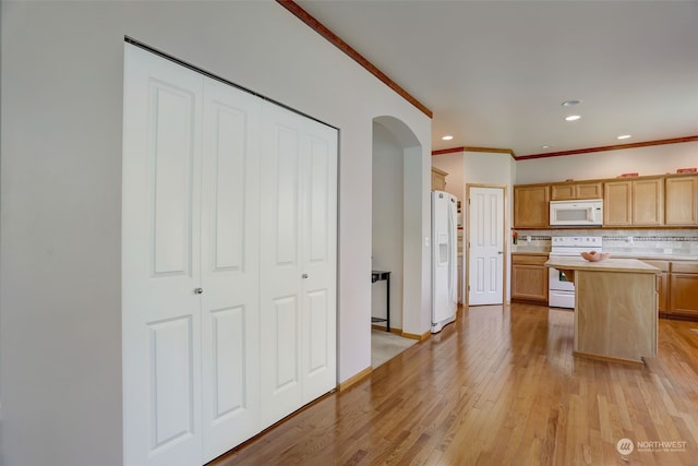 kitchen featuring white appliances, a center island, light hardwood / wood-style floors, backsplash, and ornamental molding