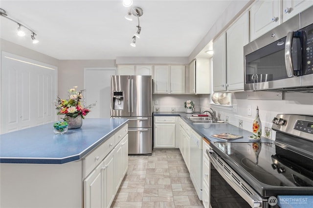 kitchen with dark countertops, a kitchen island, stainless steel appliances, white cabinetry, and a sink