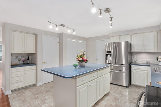 kitchen with decorative backsplash, stove, stainless steel refrigerator with ice dispenser, dark countertops, and a center island