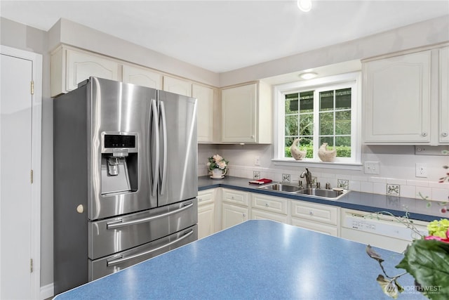 kitchen with dark countertops, stainless steel fridge with ice dispenser, white dishwasher, white cabinets, and a sink