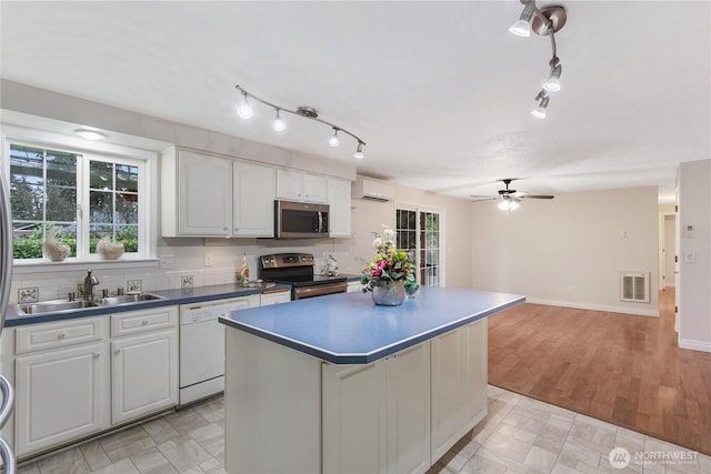 kitchen with a sink, dark countertops, a center island, stainless steel appliances, and white cabinets