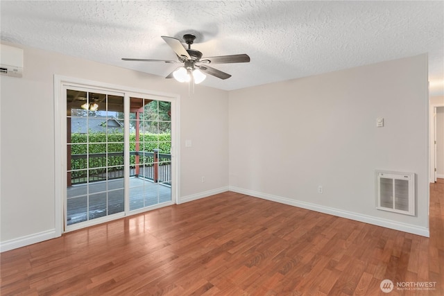 empty room with baseboards, wood finished floors, a textured ceiling, a wall mounted AC, and a ceiling fan