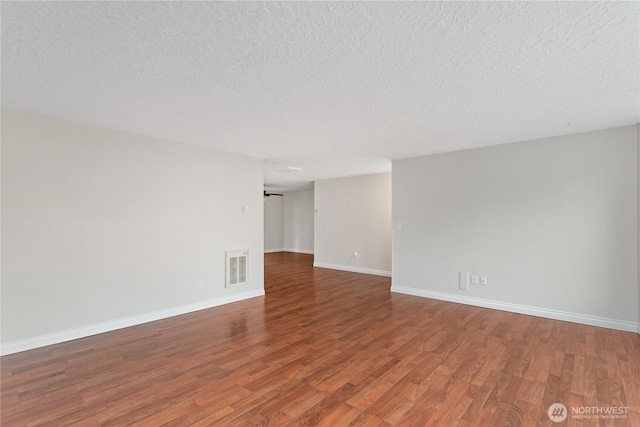 unfurnished room featuring a textured ceiling, wood finished floors, visible vents, and baseboards