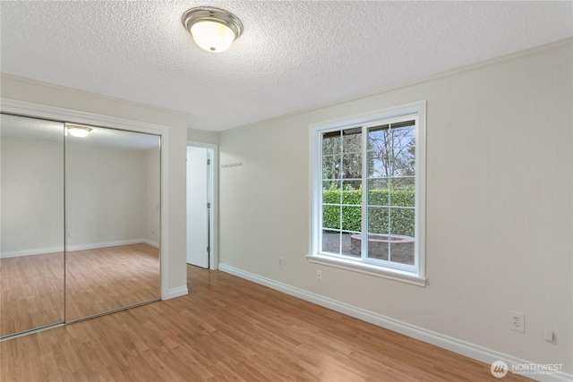 unfurnished bedroom with light wood-type flooring, a closet, baseboards, and a textured ceiling