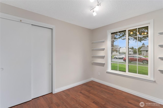 interior space featuring track lighting, a textured ceiling, wood finished floors, a closet, and baseboards