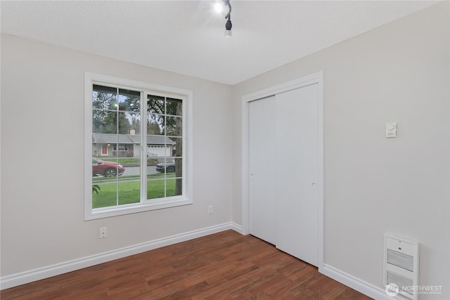 unfurnished bedroom with dark wood finished floors, heating unit, a closet, and baseboards