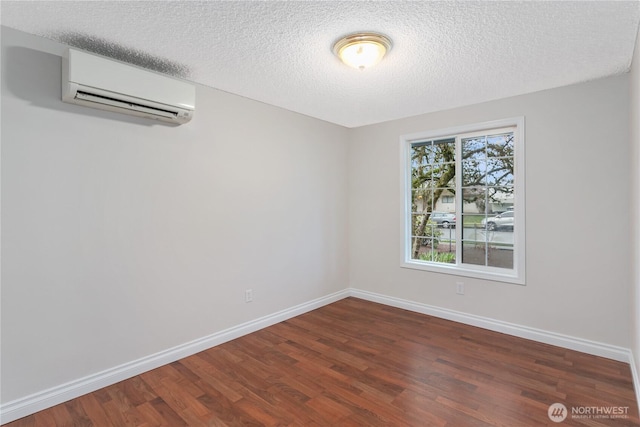 empty room with a textured ceiling, a wall mounted AC, baseboards, and wood finished floors