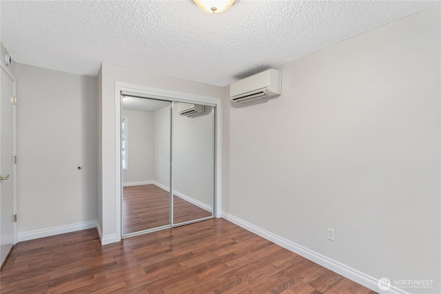 unfurnished bedroom featuring a wall mounted air conditioner, a closet, baseboards, and wood finished floors