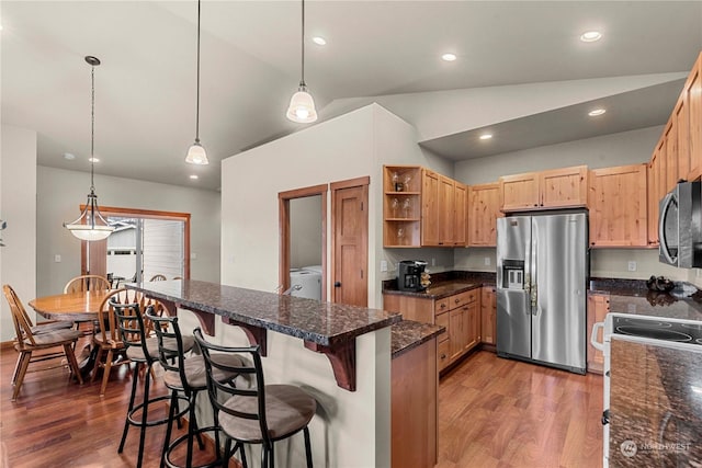 kitchen featuring appliances with stainless steel finishes, wood-type flooring, hanging light fixtures, vaulted ceiling, and washer / clothes dryer