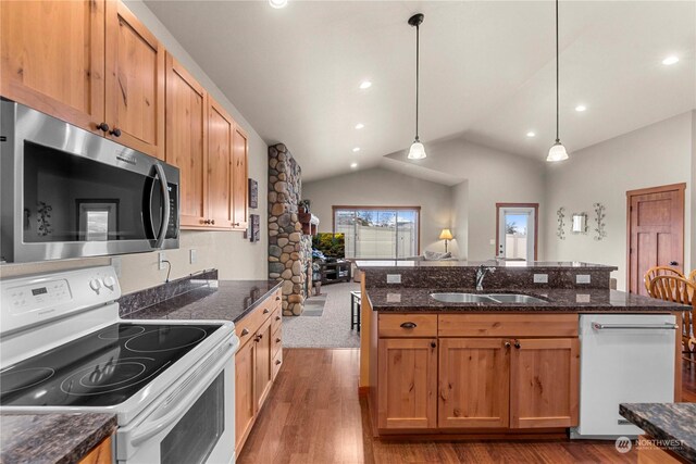 kitchen with white appliances, dark stone counters, vaulted ceiling, pendant lighting, and sink