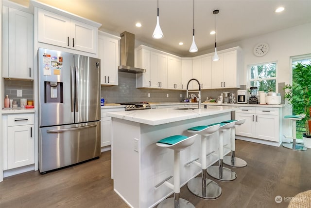 kitchen featuring appliances with stainless steel finishes, wall chimney exhaust hood, sink, decorative light fixtures, and white cabinetry