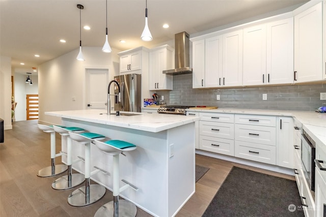 kitchen with pendant lighting, a kitchen island with sink, wall chimney exhaust hood, and stainless steel fridge with ice dispenser