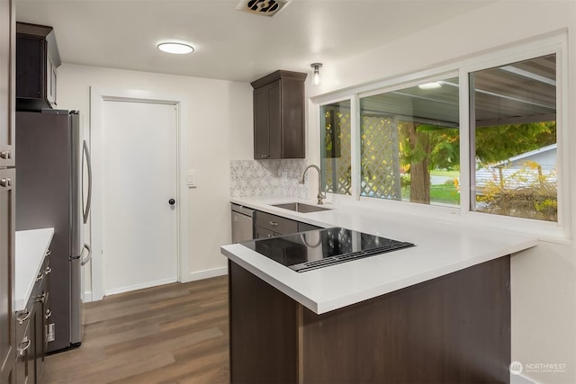 kitchen featuring sink, dark wood-type flooring, stainless steel refrigerator, dark brown cabinetry, and tasteful backsplash