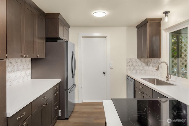 kitchen with appliances with stainless steel finishes, tasteful backsplash, sink, dark brown cabinetry, and light hardwood / wood-style floors