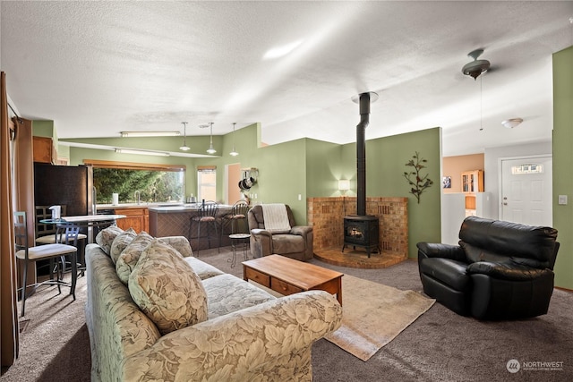 living room featuring vaulted ceiling, sink, carpet floors, a wood stove, and a textured ceiling