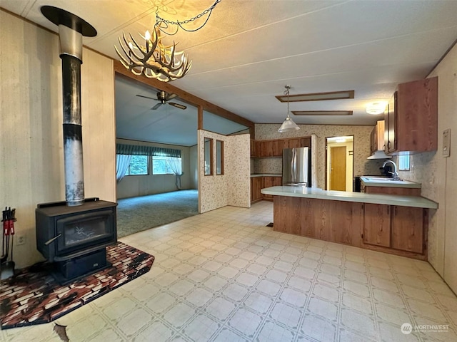 kitchen featuring ceiling fan with notable chandelier, a wood stove, sink, stainless steel fridge, and kitchen peninsula