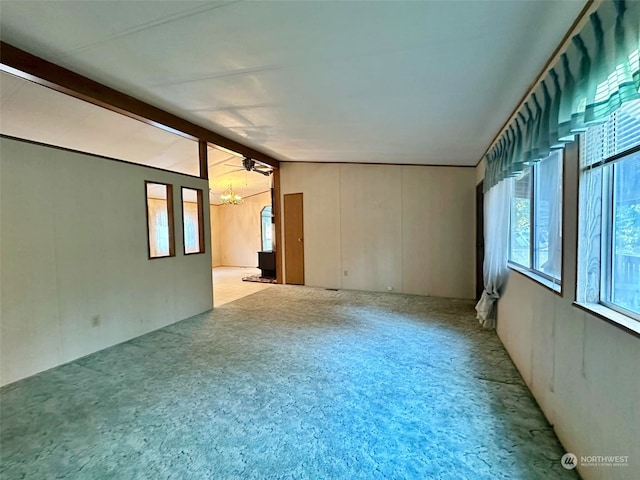 carpeted spare room with ceiling fan with notable chandelier and vaulted ceiling with beams