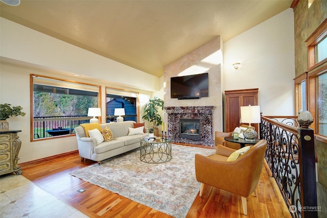 living room featuring light hardwood / wood-style floors, a wealth of natural light, a premium fireplace, and vaulted ceiling