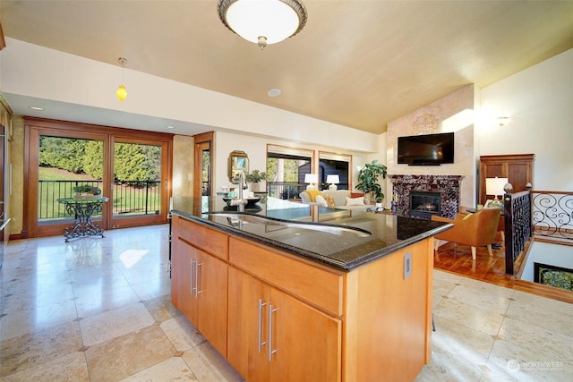 kitchen featuring a premium fireplace, dark stone counters, a wealth of natural light, and a center island with sink