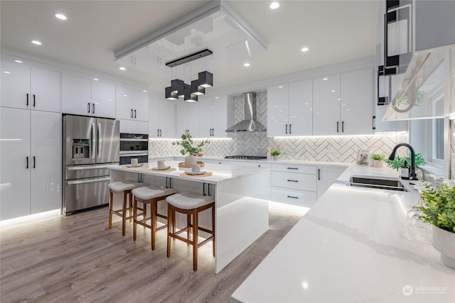 kitchen with wall chimney exhaust hood, white cabinetry, stainless steel appliances, and a kitchen island