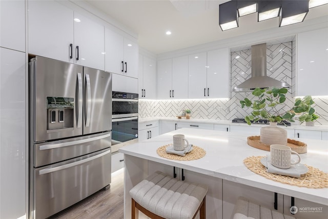 kitchen featuring a breakfast bar area, white cabinets, stainless steel appliances, range hood, and backsplash