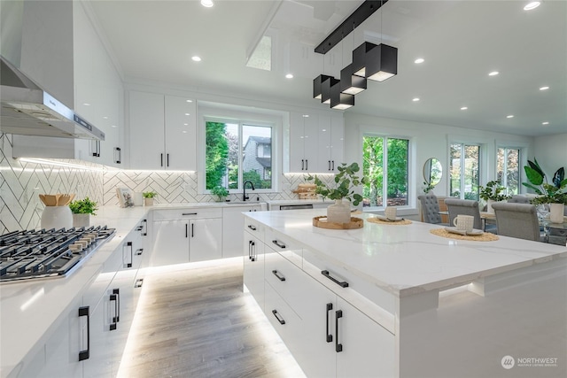 kitchen with a kitchen island, white cabinetry, stainless steel gas cooktop, light stone counters, and wall chimney exhaust hood