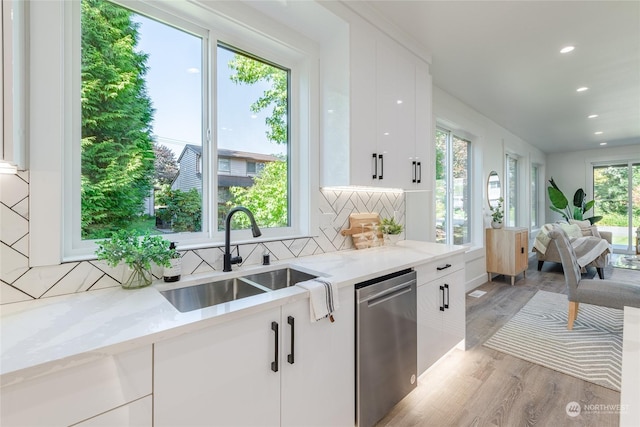 kitchen featuring light stone counters, stainless steel dishwasher, sink, and white cabinets