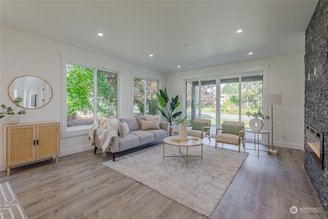 living room featuring plenty of natural light, a stone fireplace, and light hardwood / wood-style flooring