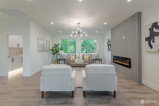 living room with an inviting chandelier, a large fireplace, and light hardwood / wood-style floors