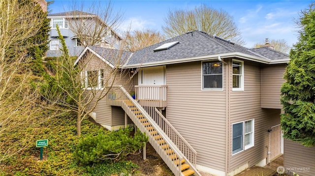 back of property with roof with shingles, a chimney, and stairs