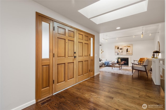 foyer entrance with dark wood-style floors, visible vents, a lit fireplace, and baseboards