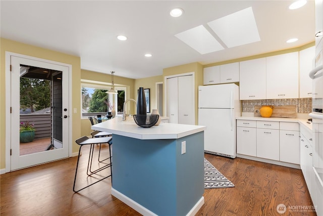 kitchen featuring a kitchen island with sink, light countertops, freestanding refrigerator, and white cabinetry