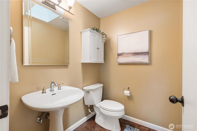 bathroom featuring a skylight, toilet, baseboards, and wood finished floors